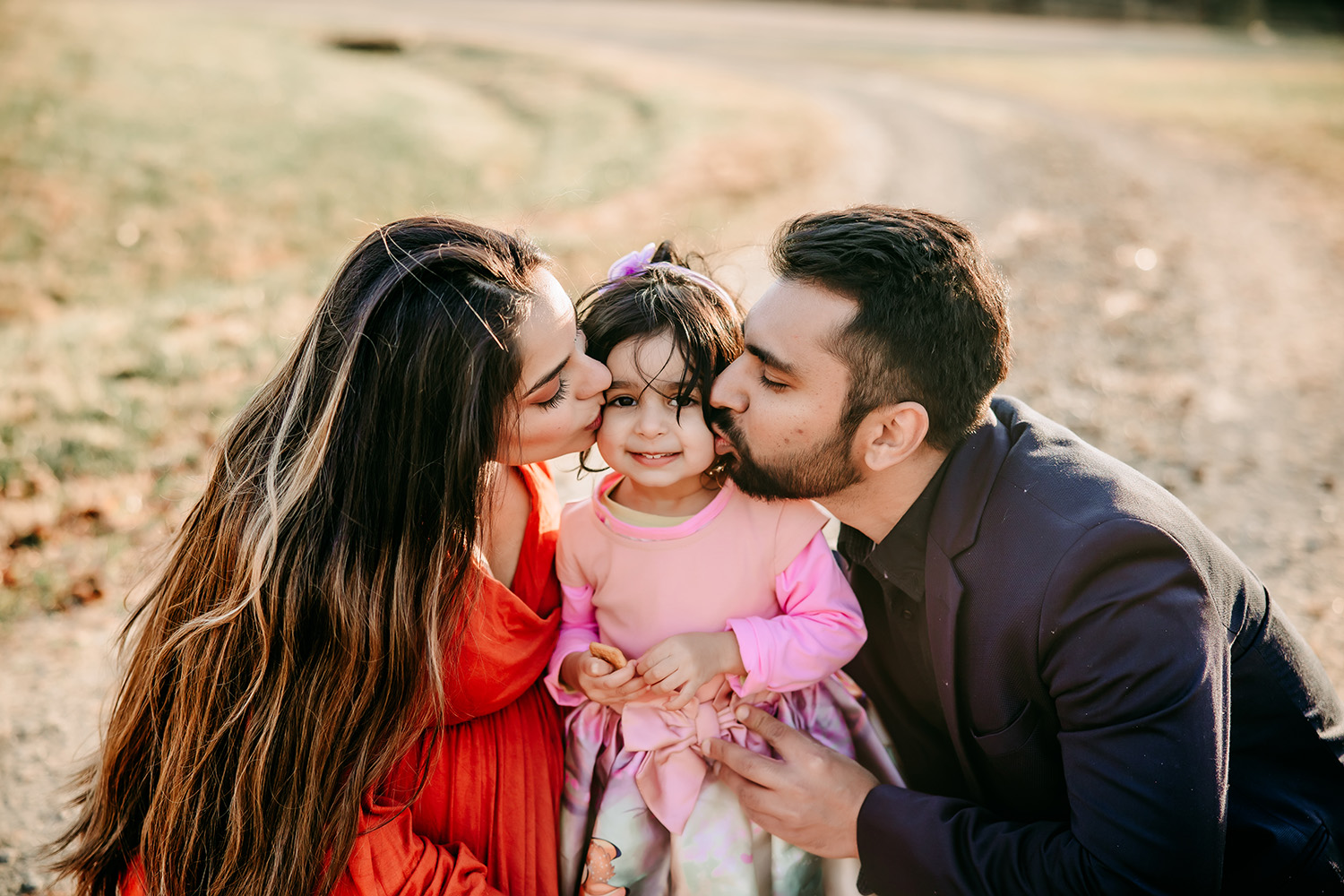 mommy-and-daddy-kissing-baby-girl-during-golden-hour-family-session-tanglewood-horse-stable-winston-salem-family-photography
