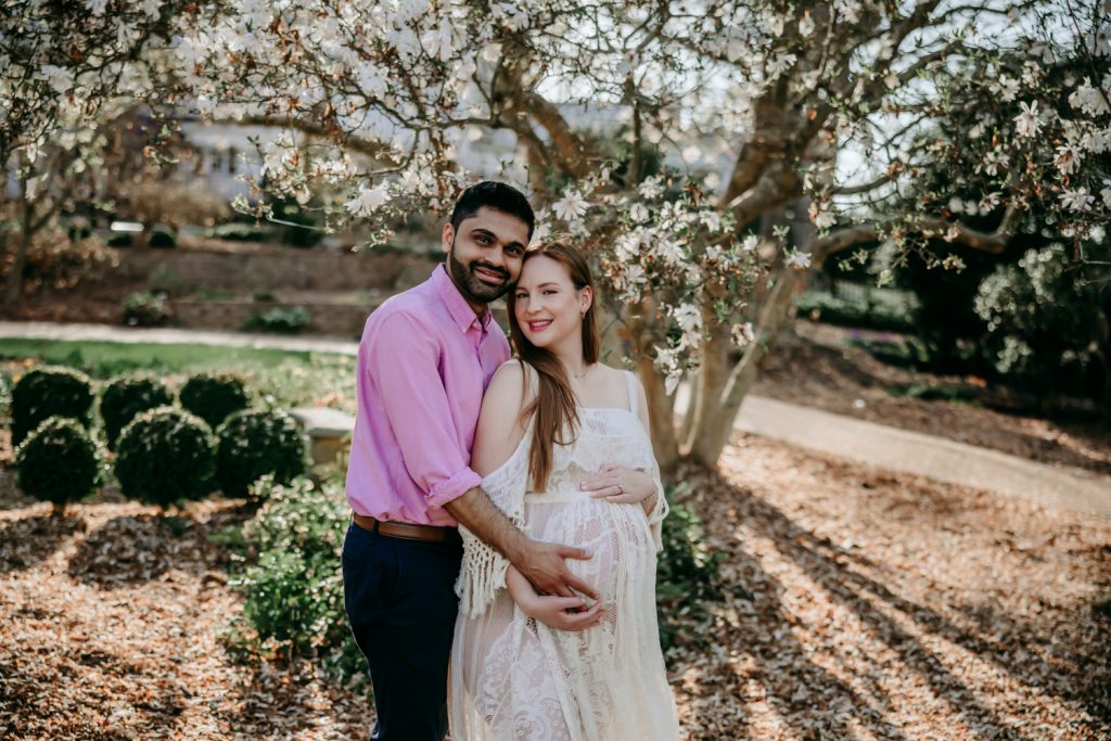 maternity mother in white lace dress with husband during golden hour maternity session in tanglewood park arboretum winston salem NC