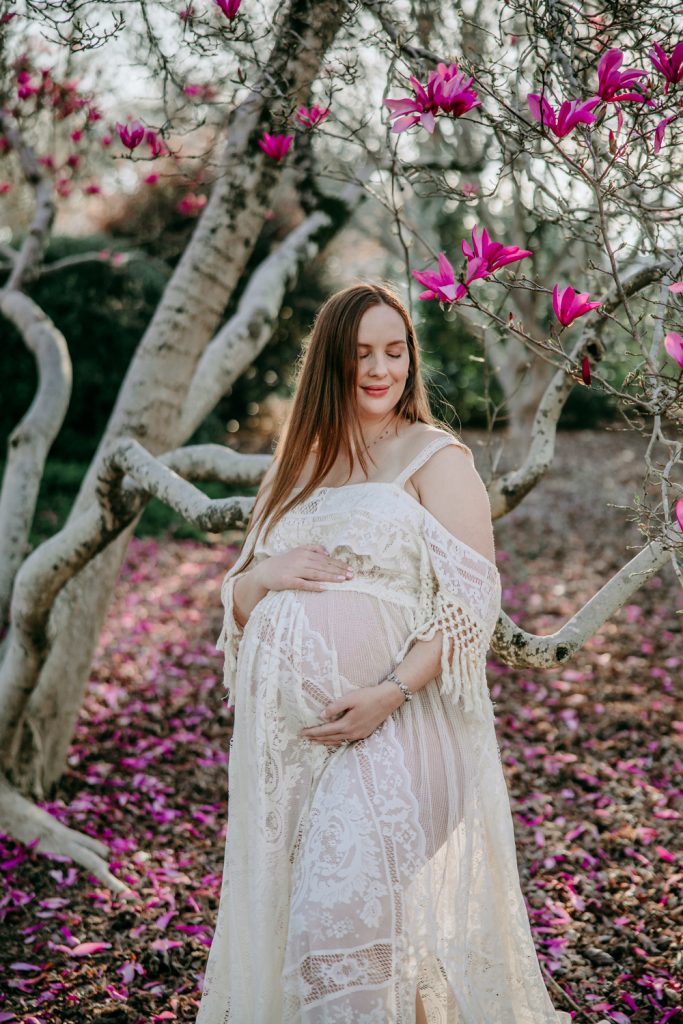 maternity mother in white lace dress under magnolia blooms in tanglewood park arboretum winston salem NC