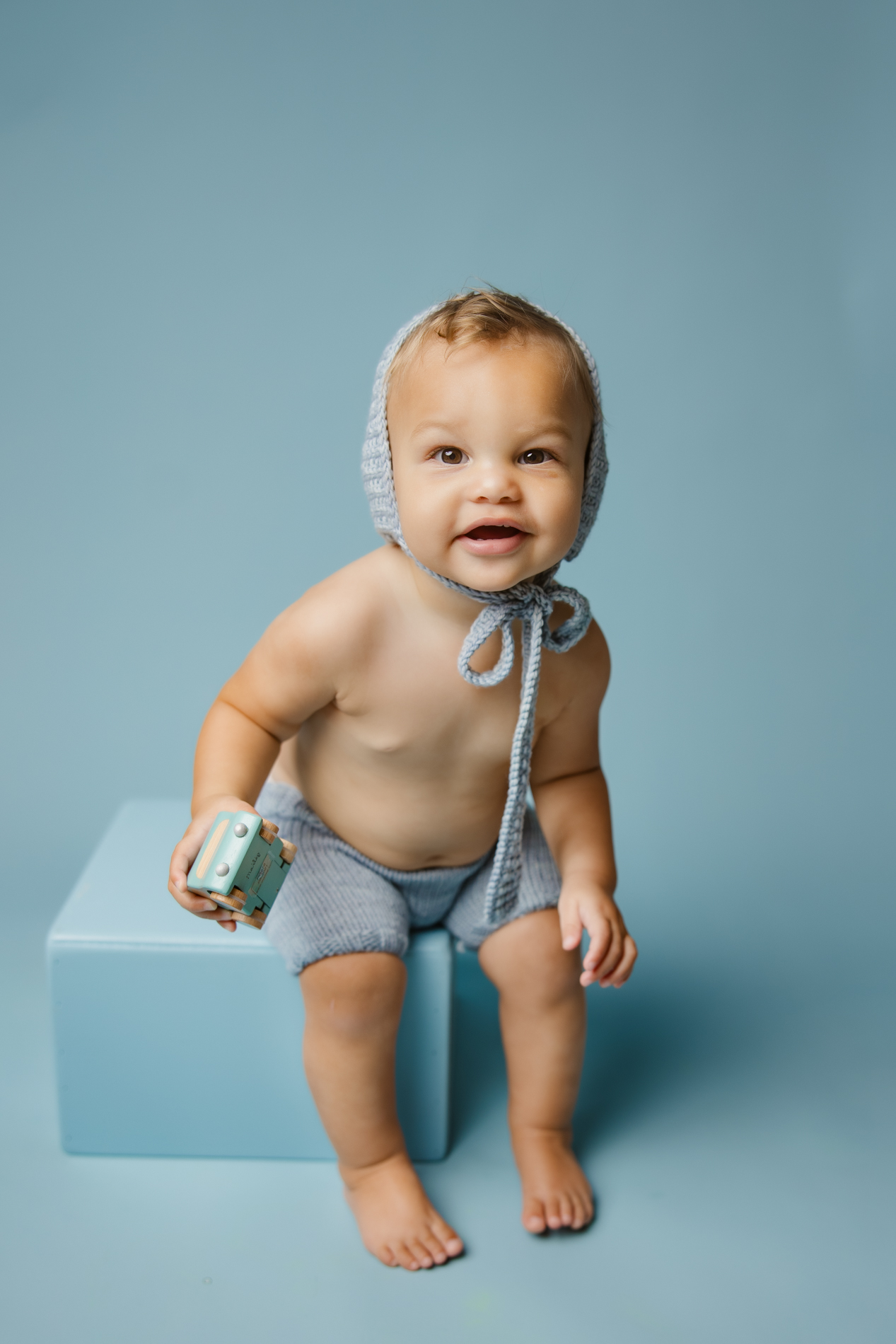 cute baby boy ginger hair in blue bonnet and shorts in blue background during baby milestone photo session Charlotte baby photographer studio