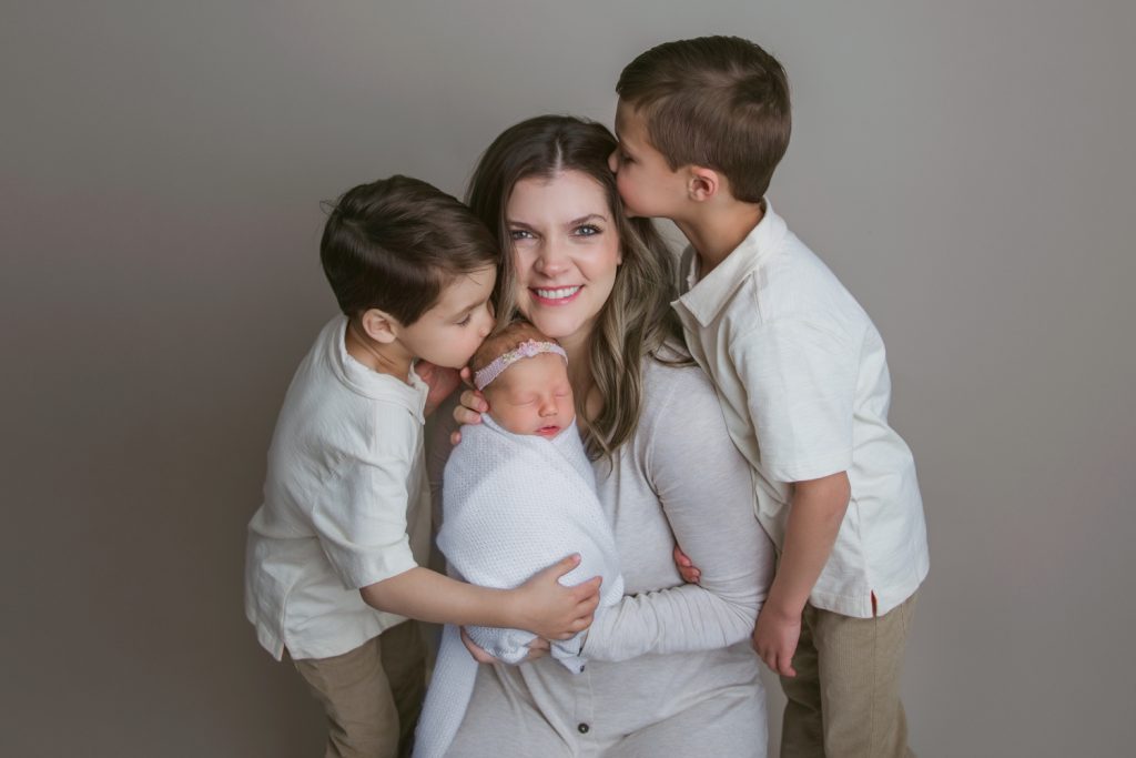 two boys kissing their mother when mom holding her newborn baby for family photo during Winston Salem newborn photography session