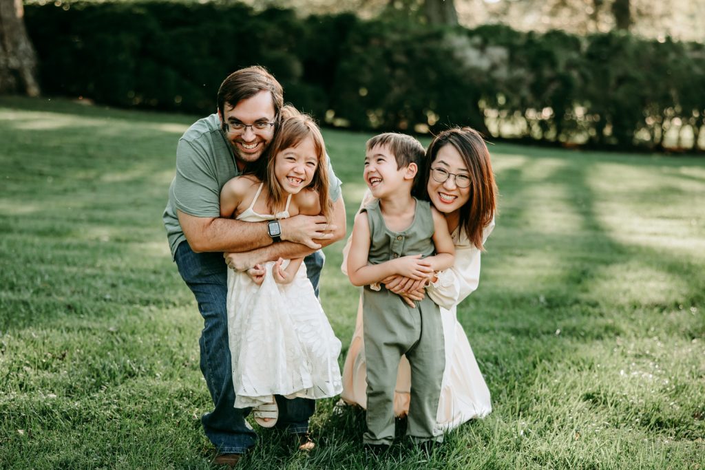 mom and dad hugging kids from behind with laughs during family photo session with greensboro family photographer