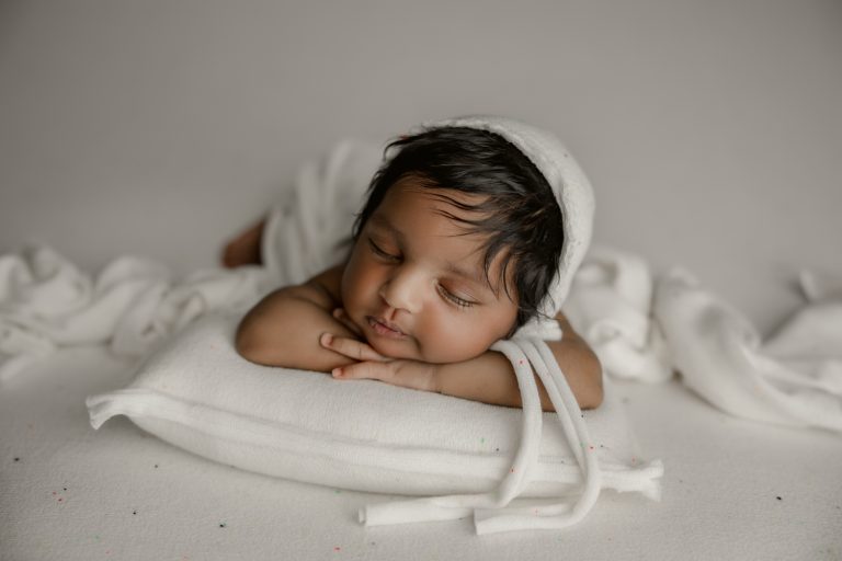 cute newborn baby girl in white bonnet sleeping and smiling on the pillow during winston-salem newborn photo session