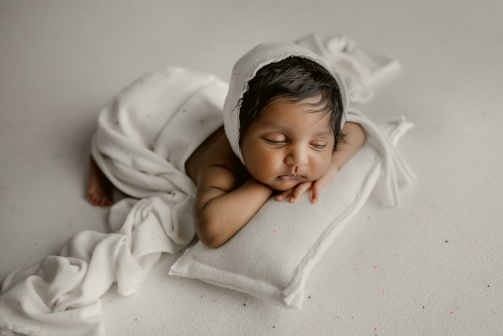 sweet newborn baby girl in white bonnet sleeping on the pillow during greensboro newborn photo session