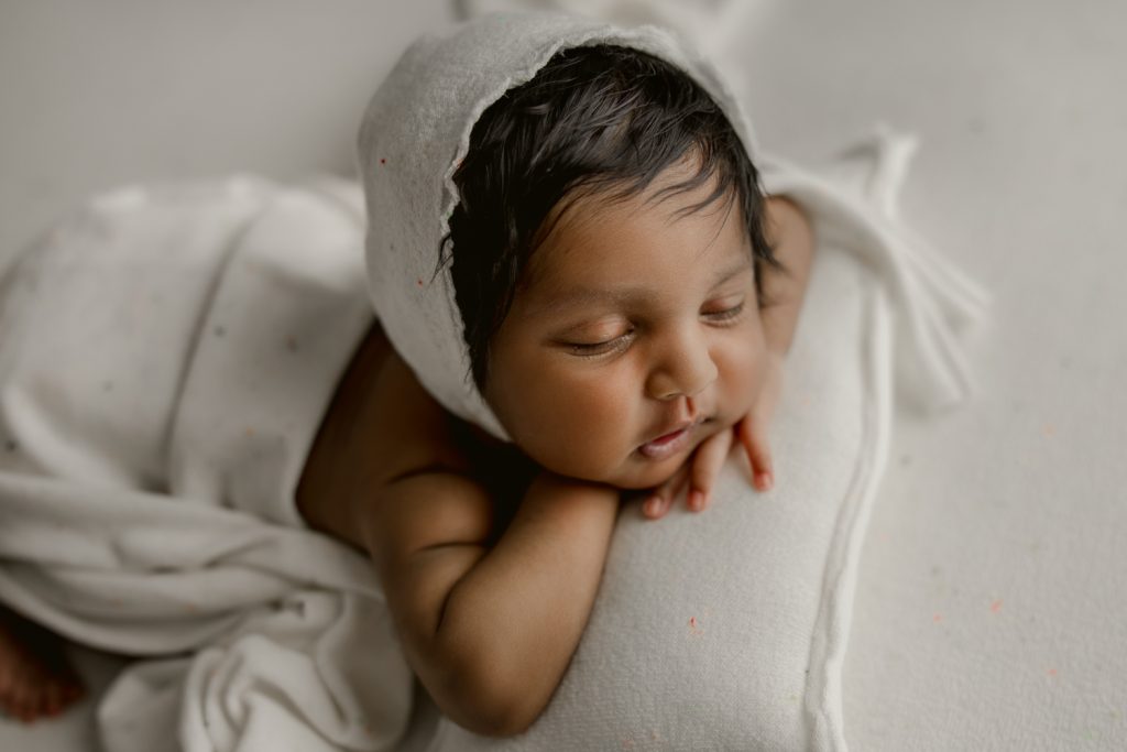 sweet newborn baby girl in white bonnet sleeping on the pillow during greensboro newborn photo session