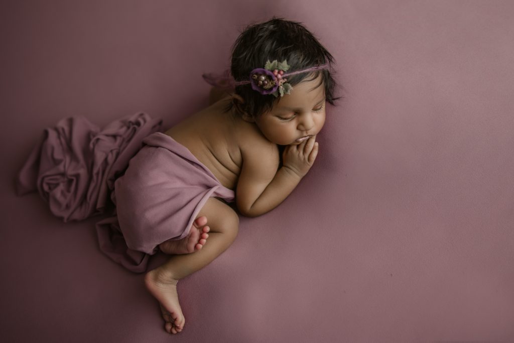 newborn baby girl sleeping on a dark berry color blanket during newborn photo session in Greensboro newborn photo studio