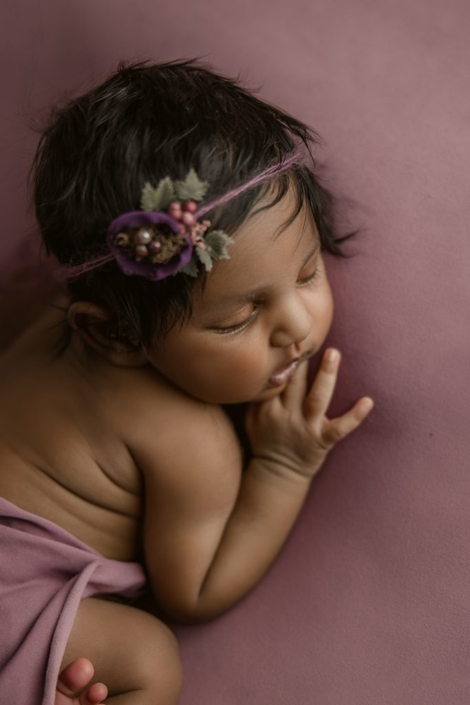 newborn baby girl with Indian heritage sleeping on a berry color blanket during newborn photo session in Winston-Salem newborn photo studio