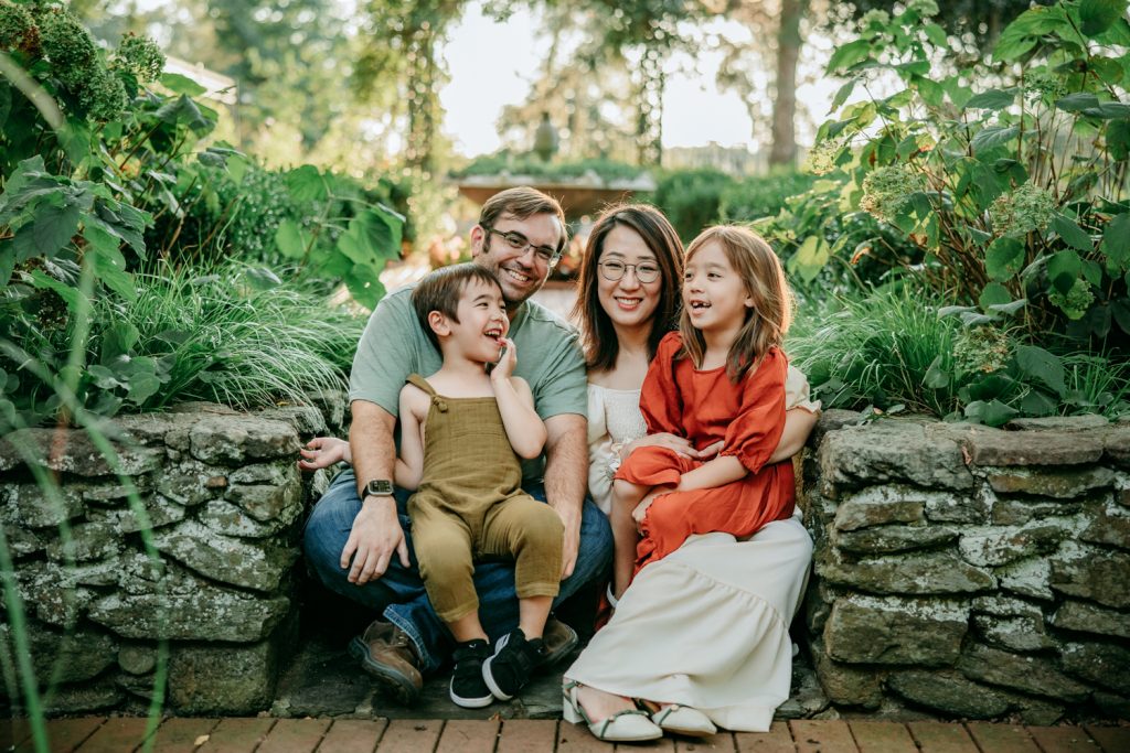 family of 4 sitting on the stone stairs during family photo session in Tanglewood botanic garden with Greensboro family photographer