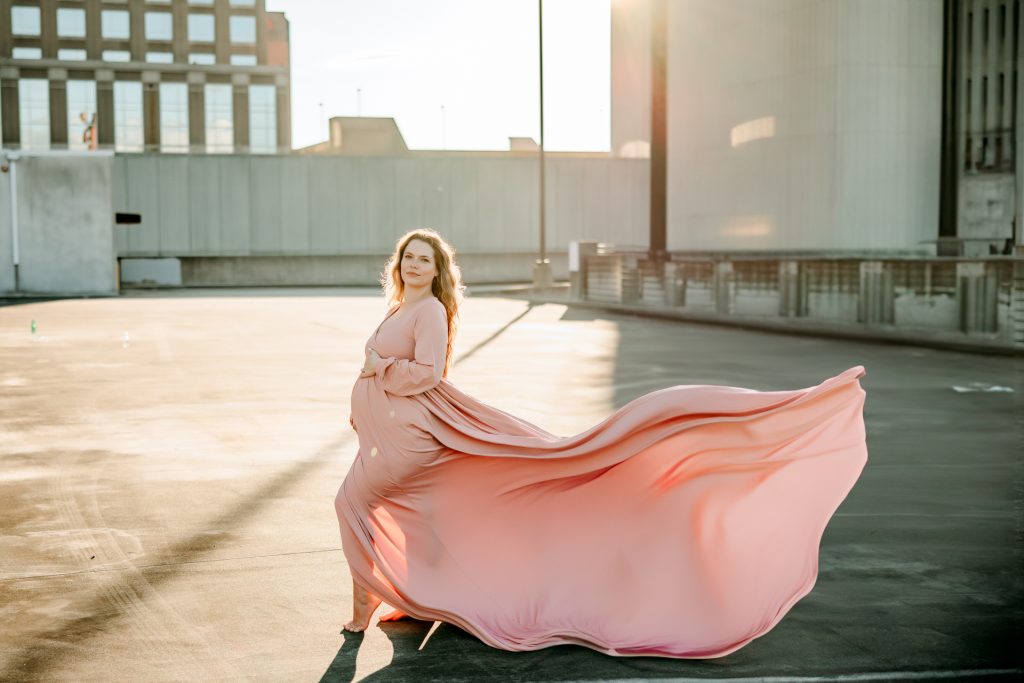 golden hour maternity photo session with expectant mother in flowy pink dress at the rooftop parking lot in downtown Winston Salem with greensboro maternity photographer
