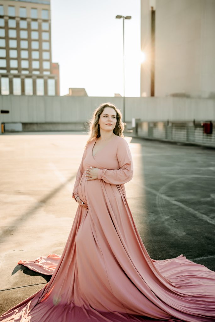 golden hour maternity photo session with expectant mother in flowy pink dress at the rooftop parking lot in downtown Winston Salem with greensboro maternity photographer