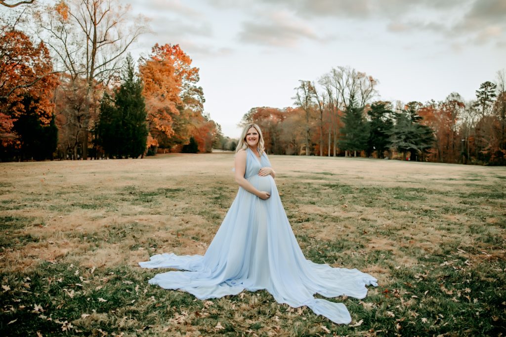 maternity mother in blue chiffon dress in the open field during family photo session in Reynolda garden with Winston salem photographer