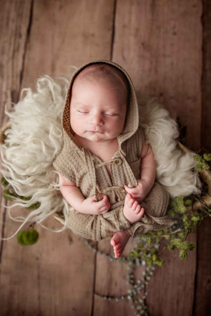newborn baby boy wearing hooded onesie sleeping in the basket during greensboro photo session