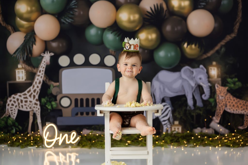 baby boy sitting on high chair eating his birthday cake during wild one themed cake smash photo session with greensboro baby photographer