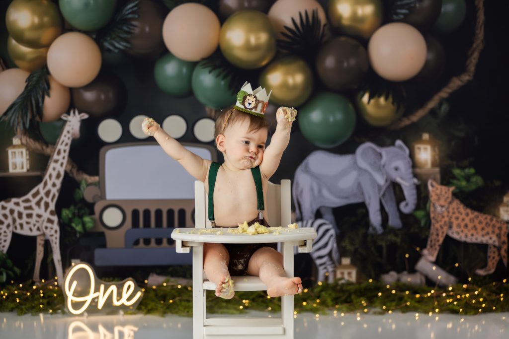baby boy sitting on high chair eating his birthday cake during wild one themed cake smash photo session with greensboro baby photographer