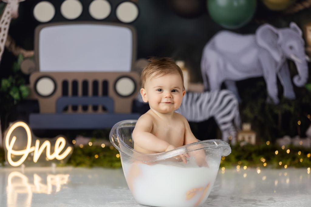 baby boy in milk bath sucking his fingers during first birthday cake smash photoshoot with greensboro baby photographer