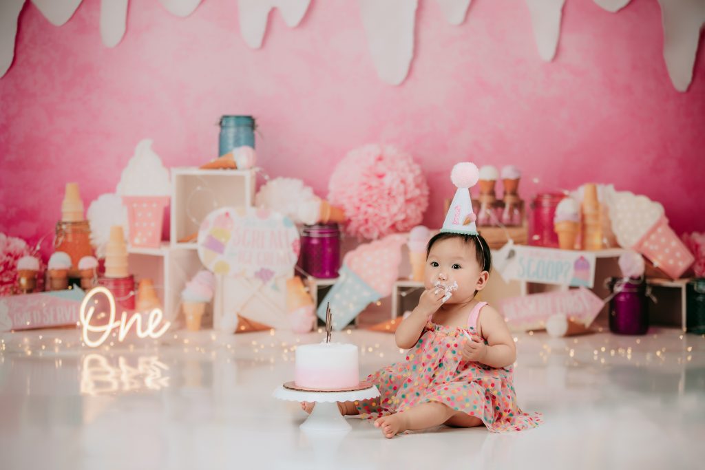 baby girl in pink poka dot dress eating cake during ice cream theme cake smash session in Winston Salem photo studio