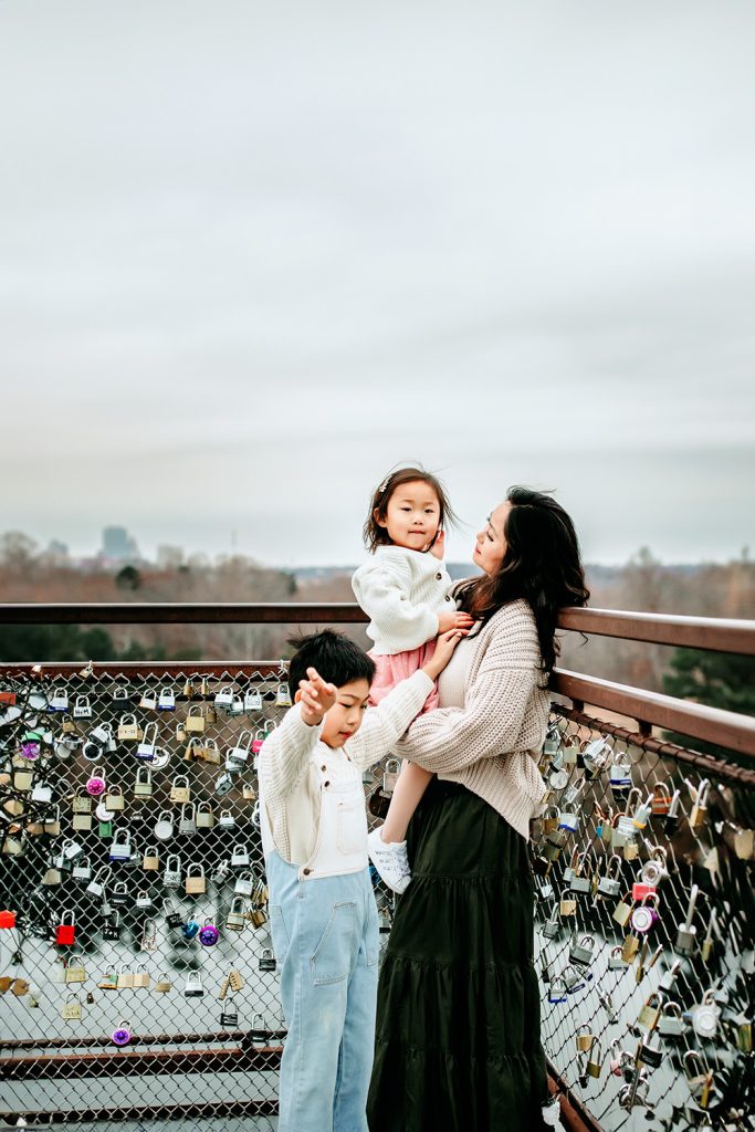 mom-holding-daughter-next-to-son-on-the-bridge-during-family-photo-session-at-quarry-park-in-winston-salem