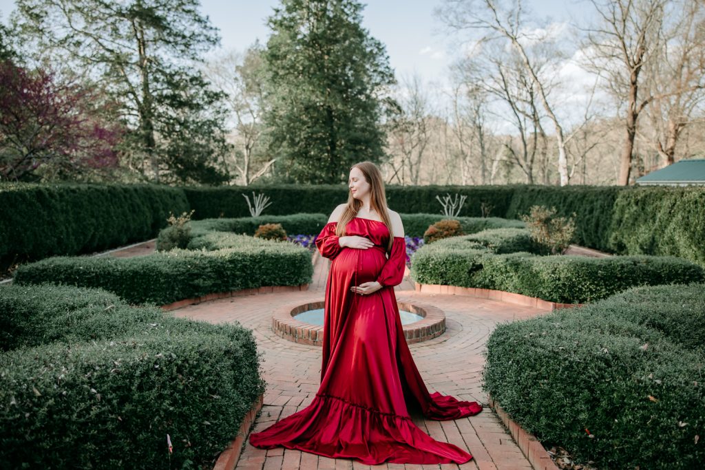 beautiful-expectant-mother-in-flowy-red-gown-in-tanglewood-park-garden-during-maternity-photo-session-with-winston-salem-motherhood-photographer