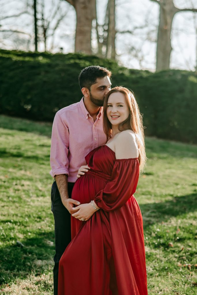 husabnd-kissing-his-beautiful-expectant-mother-in-flowy-red-gown-in-tanglewood-park-garden-during-maternity-photo-session-with-winston-salem-motherhood-photographer