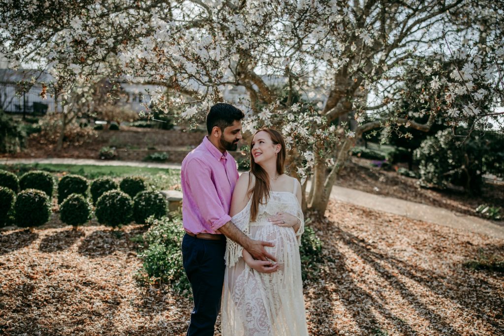 maternity-mother-in-white-lace-dress-with-husband-during-golden-hour-maternity-photo-session-in-tanglewood-park-arboretum-winston-salem-NC