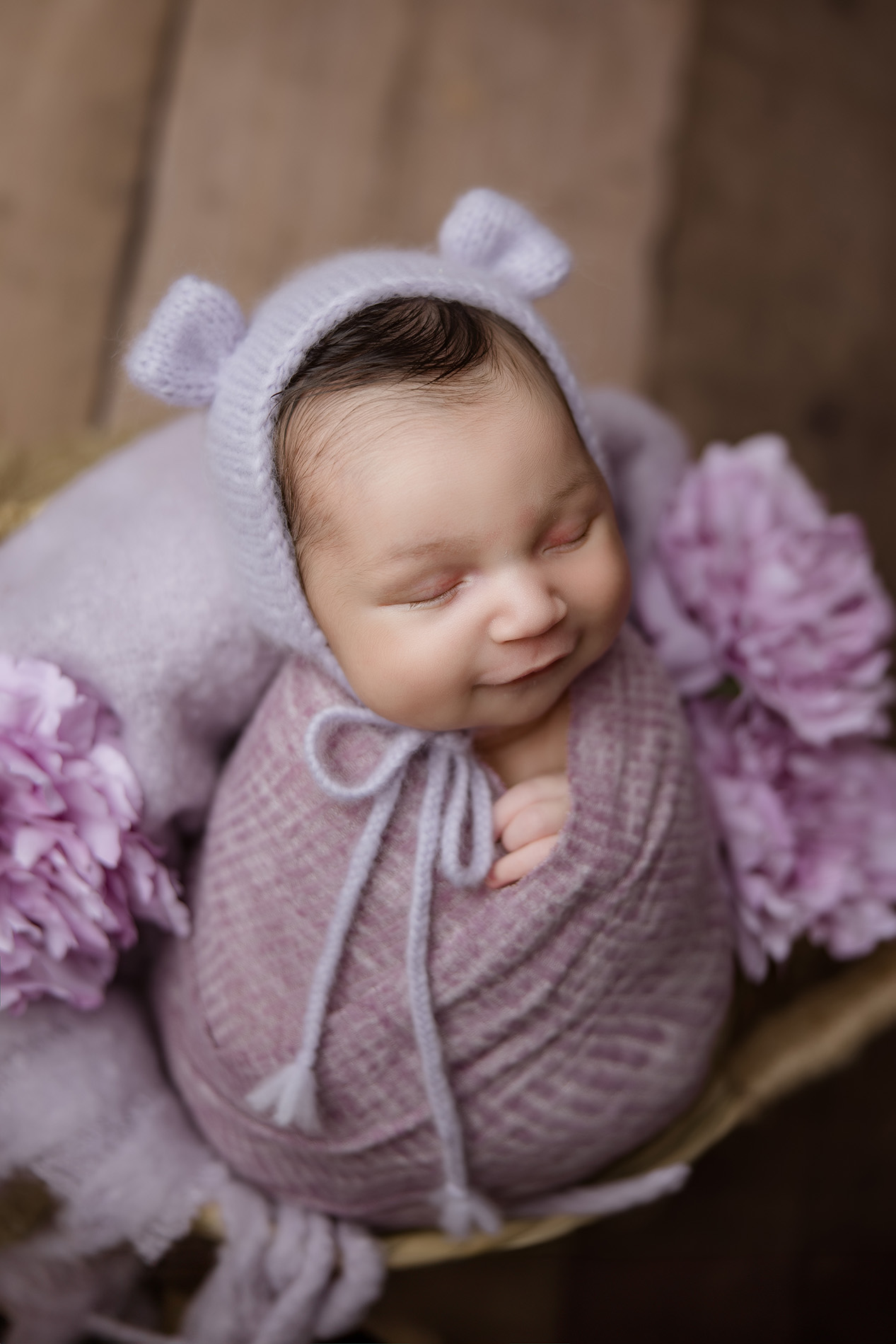 smiling-newborn-baby-girl-swaddled-in-lilac-color-sitting-in-floral-basket-during-greensboro-newborn-photography-session