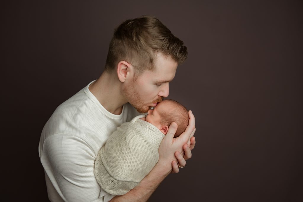 dad-holding and kissing-his-newborn-baby-twins-in-family-photo-during-winston-salem-newborn-photography-session