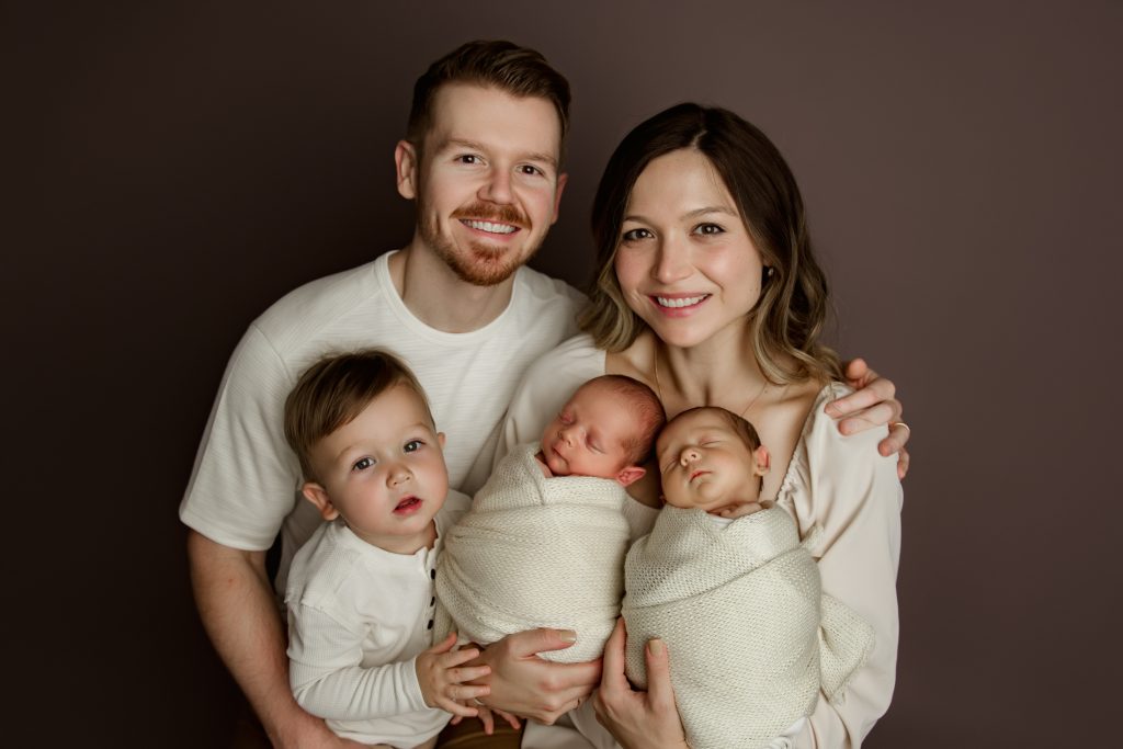 mom-and-dad-holding-their-newborn-baby-twins-and-toddler-brother-in-family-photo-during-winston-salem-newborn-photography-session