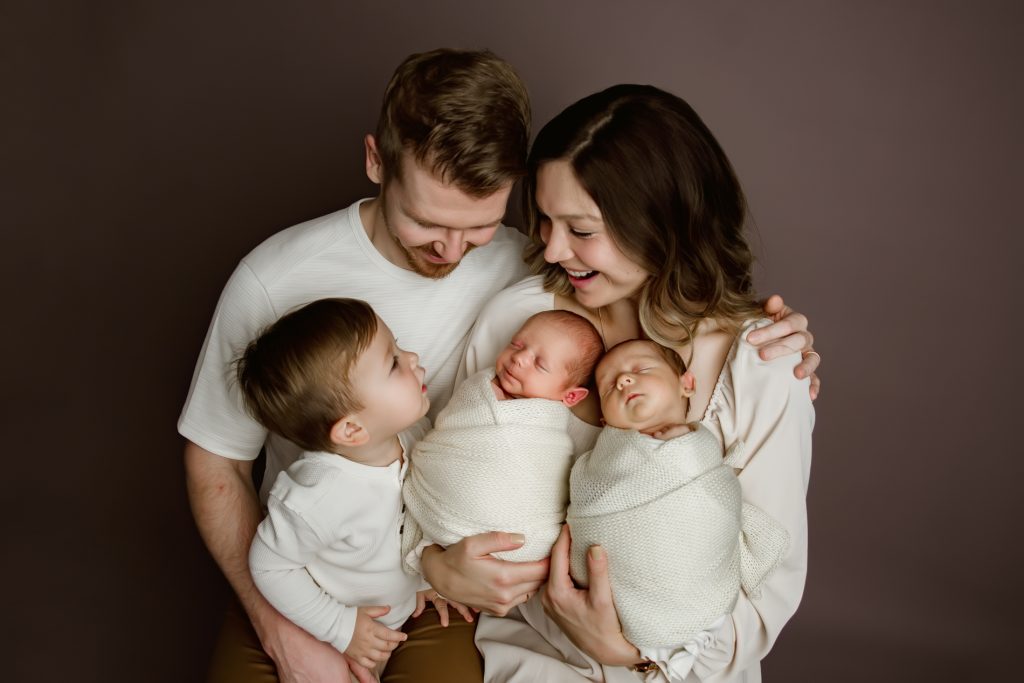 mom-and-dad-holding-their-newborn-baby-twins-and-toddler-brother-in-family-photo-during-winston-salem-newborn-photography-session