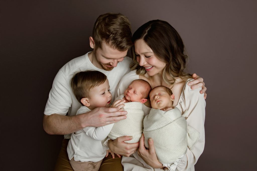 mom-and-dad-holding-their-newborn-baby-twins-and-toddler-brother-in-family-photo-during-winston-salem-newborn-photography-session