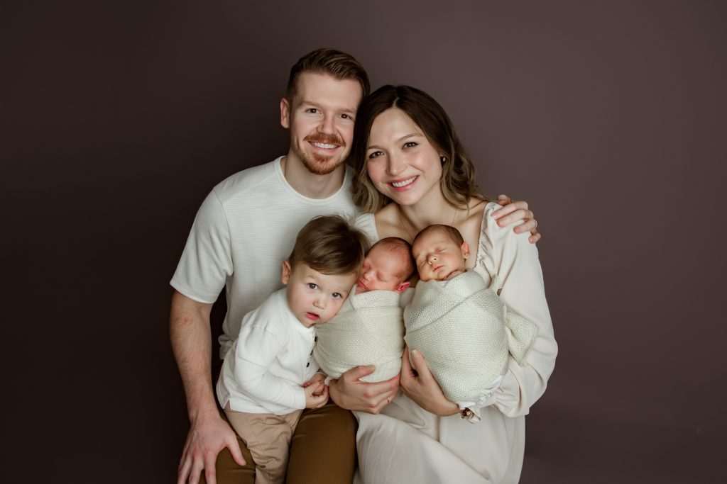 mom-and-dad-holding-their-newborn-baby-twins-and-toddler-brother-in-family-photo-during-winston-salem-newborn-photography-session