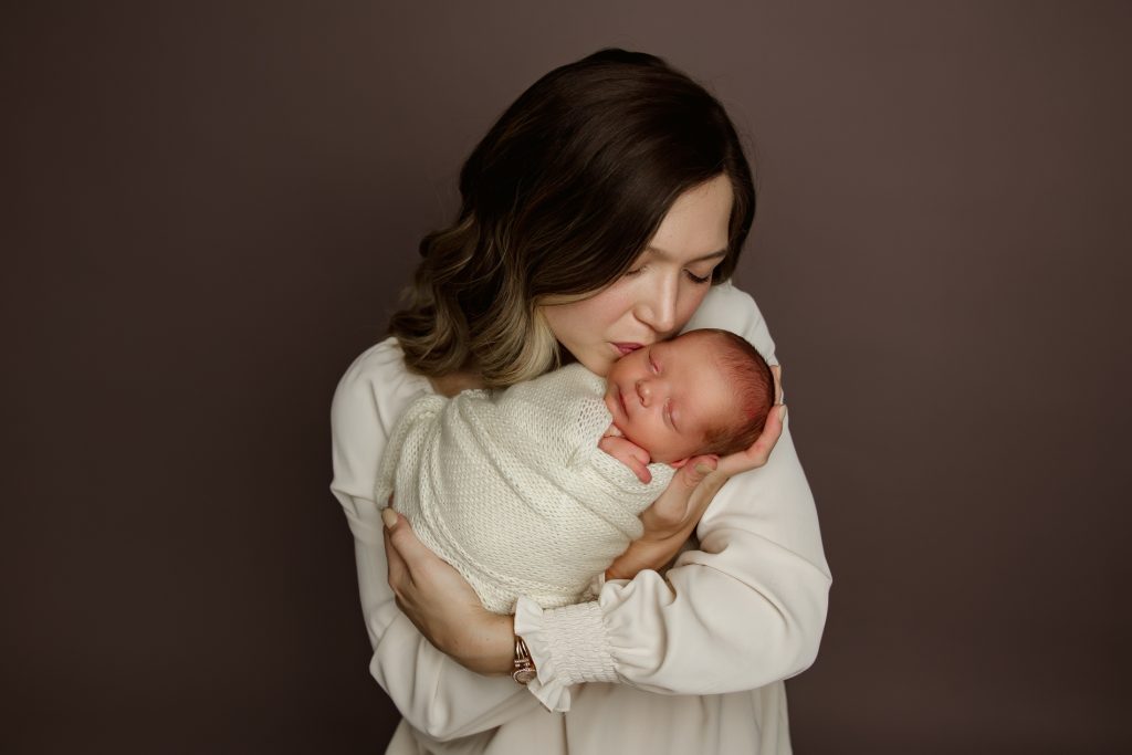 mother-holding-and-kissing-her-newborn-baby-in-family-photo-during-winston-salem-newborn-photo-session