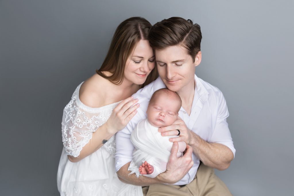 parents holding sleeping newborn baby boy eyes closed for family photo during newborn photo sessions with Winston Salem newborn photographer