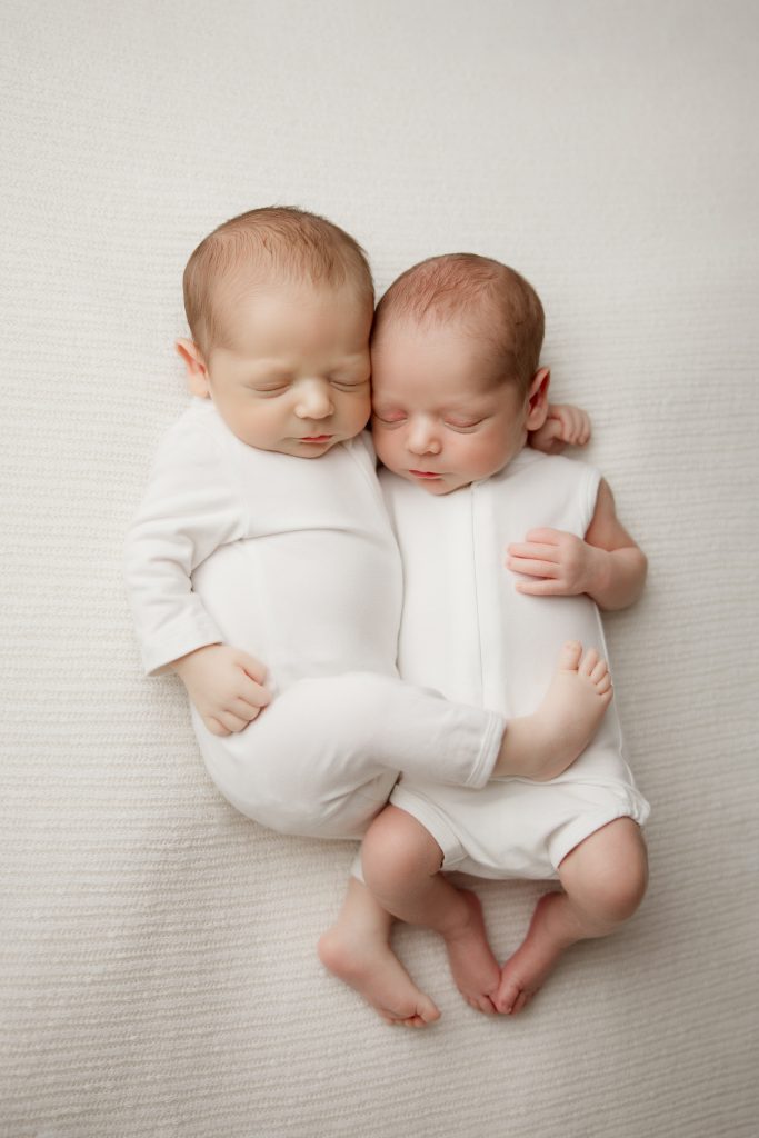 newborn-twin-boys-hugging-each-other-sleeping-in-white-blanket-during-winston-salem-newborn-photography-session