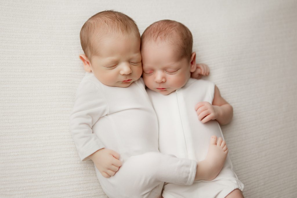 newborn-twin-boys-hugging-each-other-sleeping-in-white-blanket-during-winston-salem-newborn-photography-session