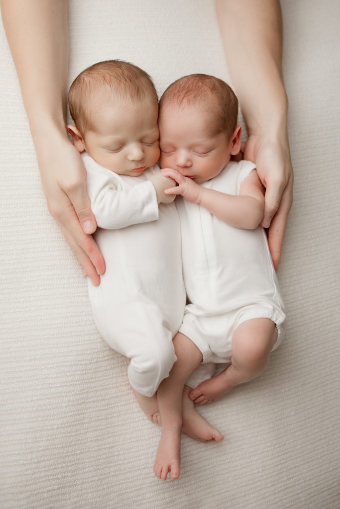 newborn-twin-boys-hugging-each-other-sleeping-in-white-blanket-during-winston-salem-newborn-photography-session