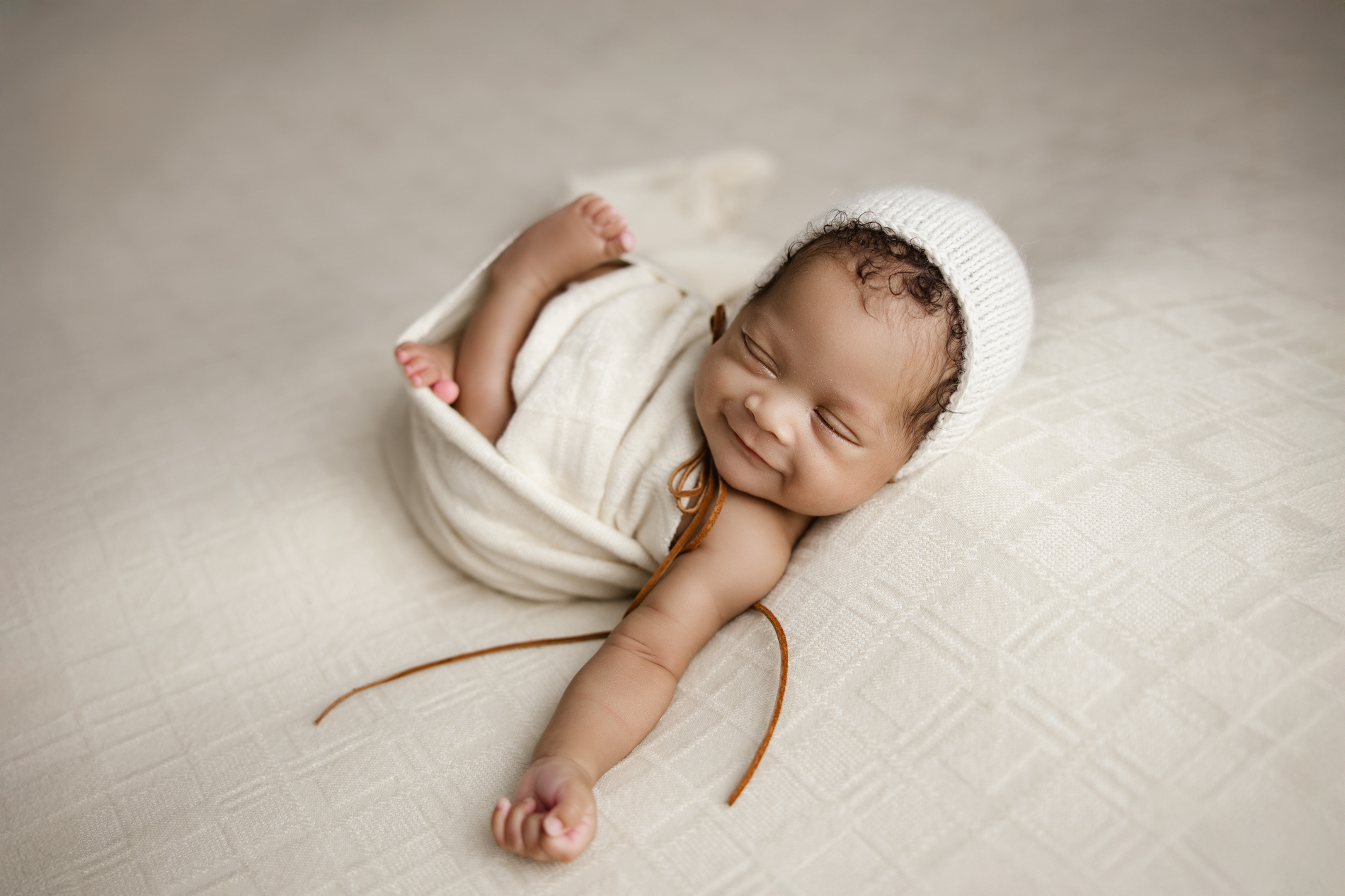 smiling-newborn-baby-boy-in-white-bonnet-in-sleep-during-newborn-photo-session-winston-salem-NC-photography-studio