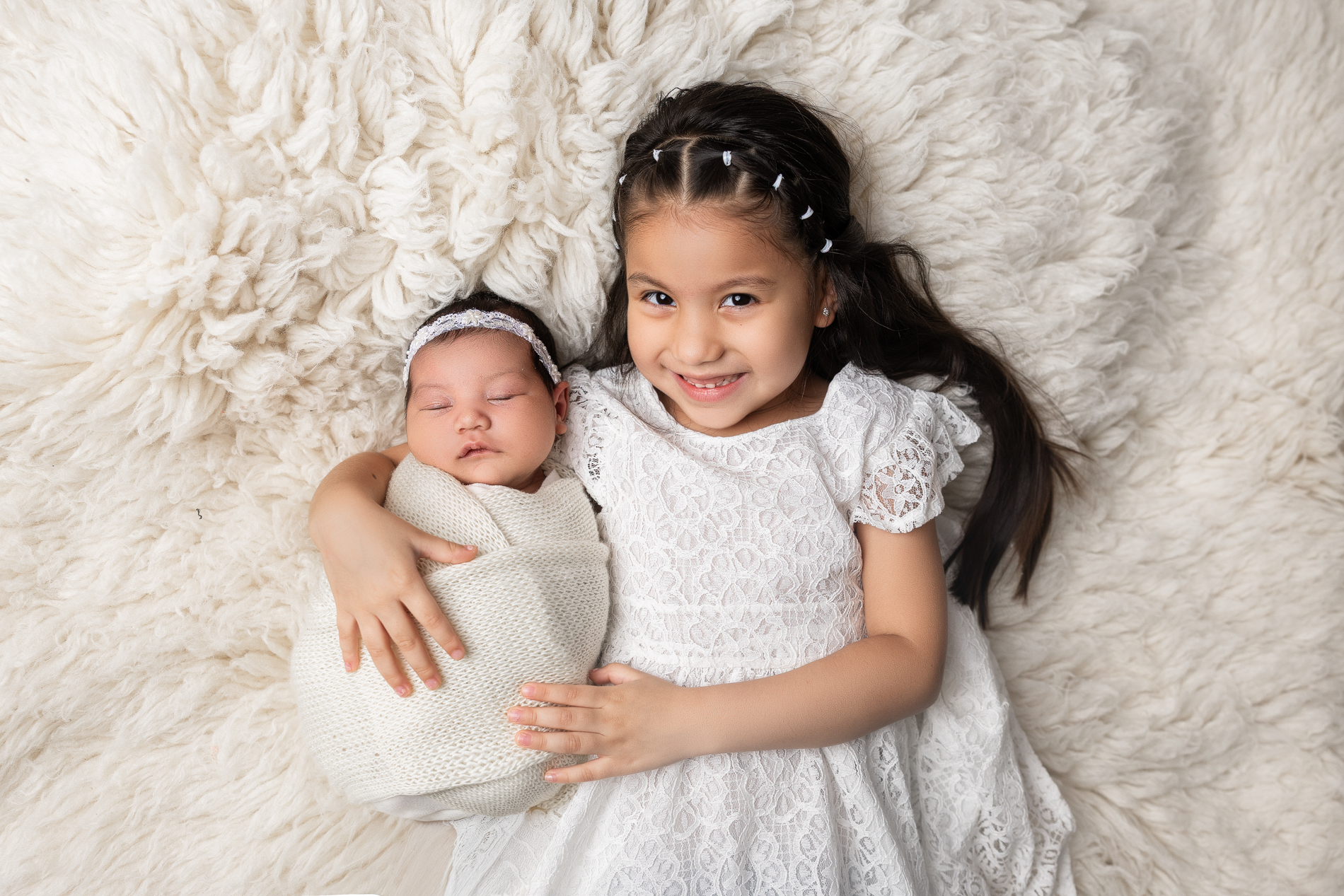 little-girl-holding-her-baby-sister-laying-on-white-blanket-during-greensboro-newborn-photo-session