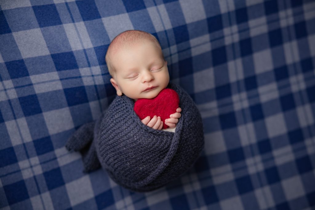 newborn-baby-boy-sleeping-in-a-checked-navy-blue-blanket-in-holding-blue-teddy-bear-and-red-heart-during-winston-salem-newborn-photography-session