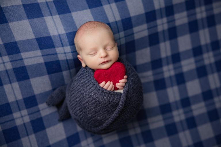 newborn-baby-boy-sleeping-in-a-checked-navy-blue-blanket-in-holding-blue-teddy-bear-and-red-heart-during-winston-salem-newborn-photography-session