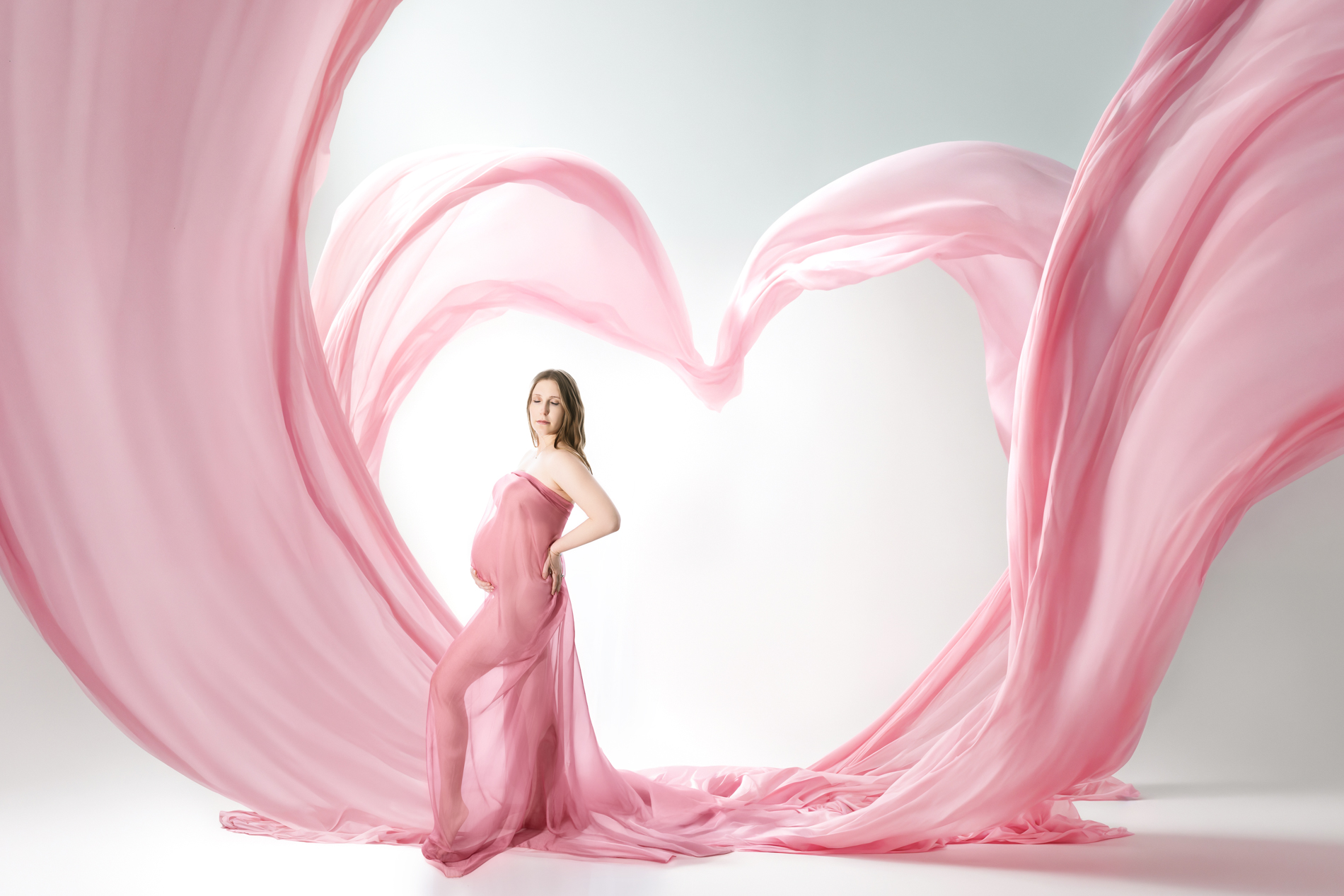 maternity-mother-wrapped-in-pink-fabric-under-giant-heart-shaped-fabric-backlit-fine-art-portrait-greensboro-maternity-photographer