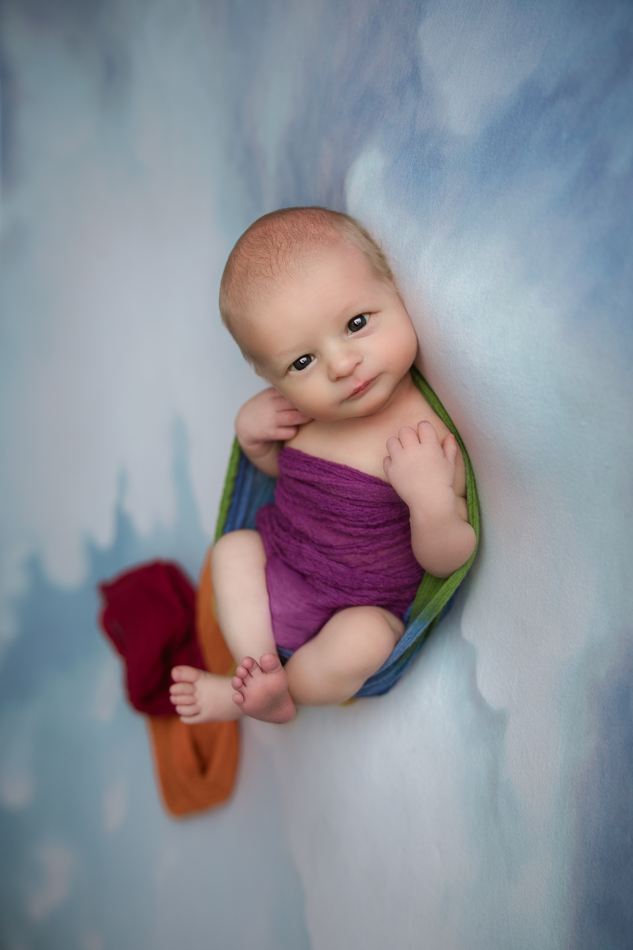 newborn-baby-boy-in-cloud-blanket-wrapped-in-rainbow-scarf-during-winston-salem-newborn-photography-session